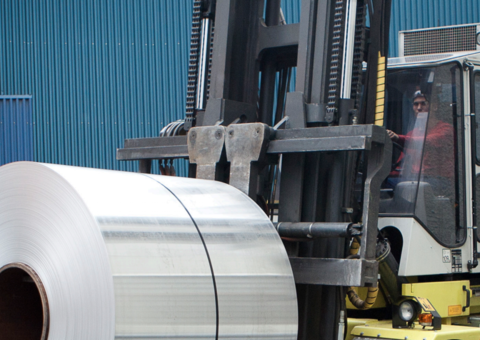 An person operating a lifttruck carrying a metal roll.