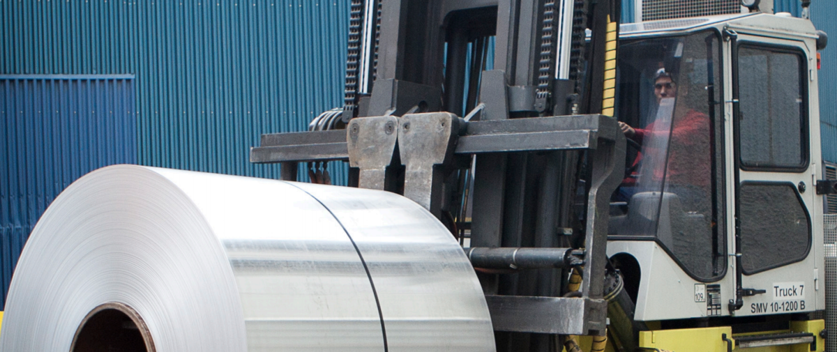 An person operating a lifttruck carrying a metal roll.